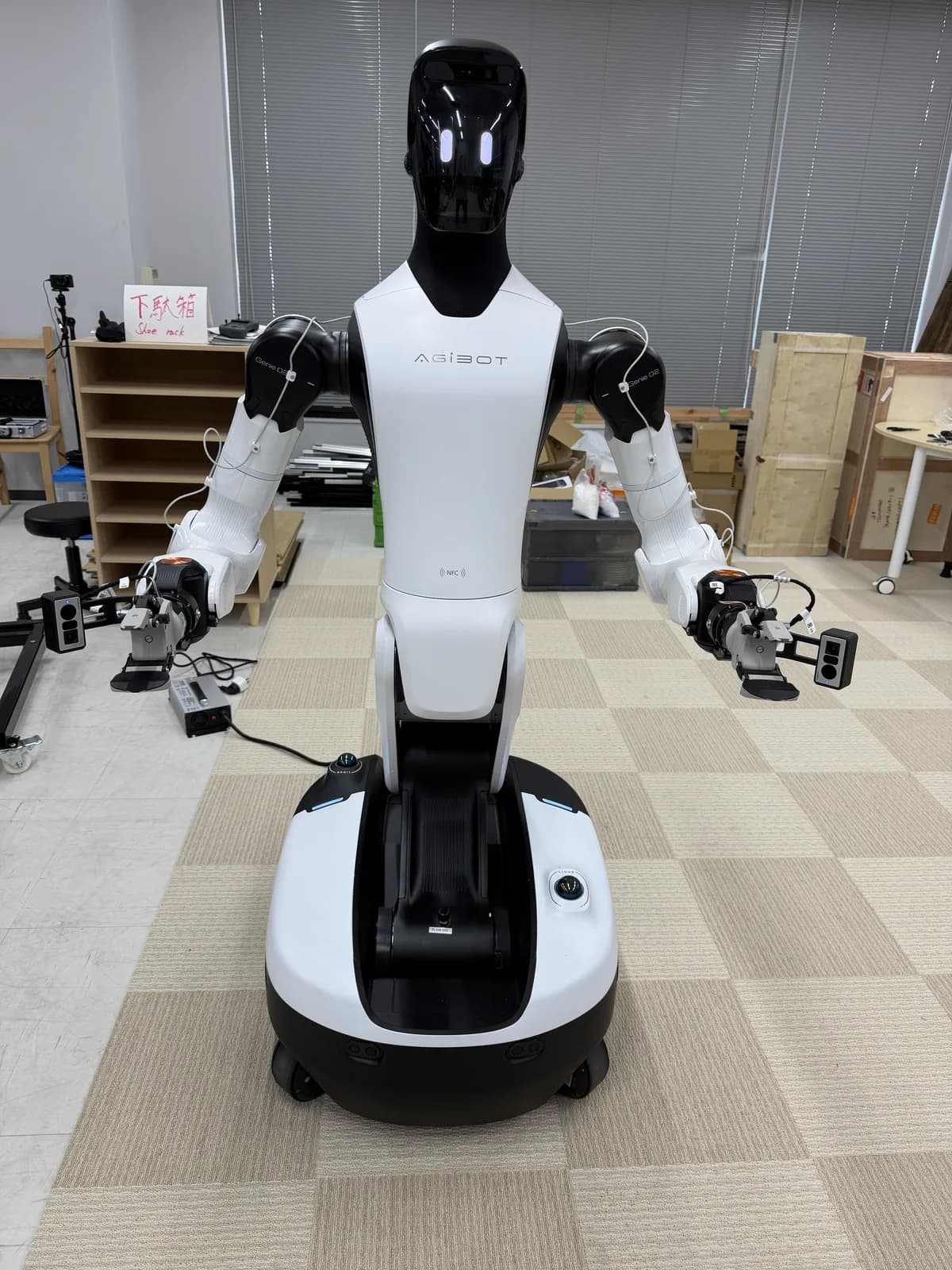 The whole body of AgiBot G2 delivered to the office. It has a black head, two white arms, and a mobile base with wheels.