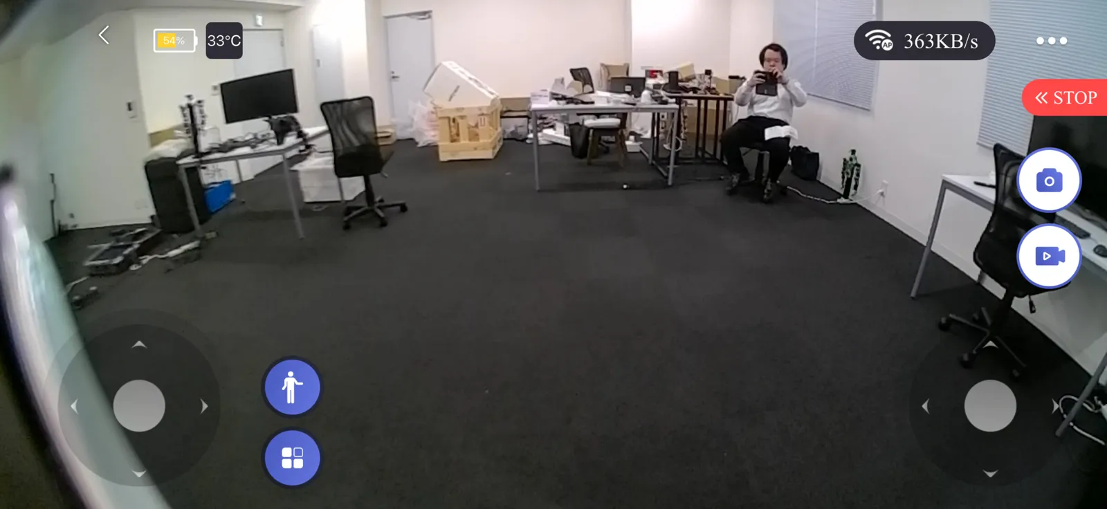 Unitree R1の頭部カメラ映像を映した操作アプリの画面。オフィスを広角で捉え、左右に移動用のスティックが表示されている
